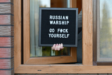 Hand holding a letterbox in the window with citation "Russian warship go f#ck yourself". War in Ukraine.