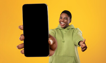 Happy african american oversized woman demonstrating cellphone with blank screen and showing thumb...