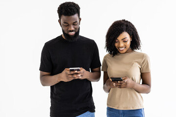 Attractive african ethnicity couple hold smart phones having fun in internet isolated on gray studio background