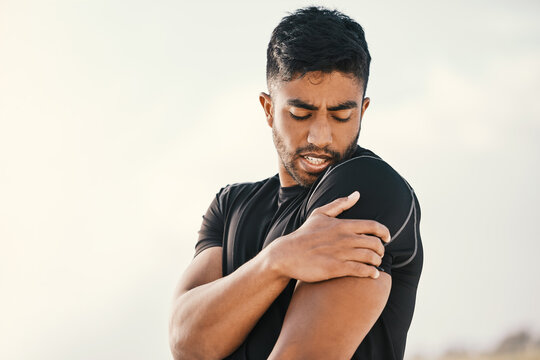 Injury Will Curtail Any Workout. Cropped Shot Of A Handsome Young Male Athlete Holding His Shoulder In Pain While Exercising On The Beach.