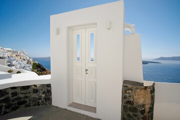 Typical design white decoration door next to an alley with a breathtaking view of the volcano and the aegean sea in Fira Santorini