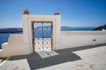 An external decorated door with flower plants on the roof of a villa and view  of the Fira and the  aegean sea in  Santorini