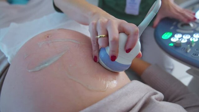 Hand of a doctor holding ultrasonic device moves by the big pregnant belly of a patient. Close up. Ultrasound check up concept.