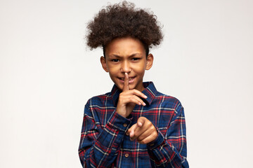 Frustrated dark-skinned handsome male kid in plaid shirt pointing at camera putting right index...