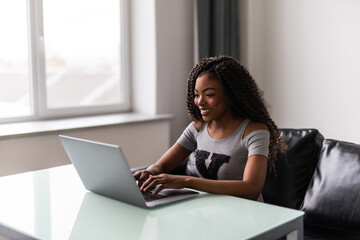 Successful african american young woman using and typing on laptop in modern office.