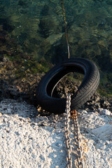 Tire tied to the sea with a chain. Clear stony sea. Rusted chain.
