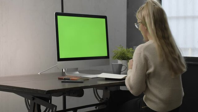 College student watching lesson online and studying from home. Young woman taking notes while looking at computer screen following professor doing math on video call. Green screen