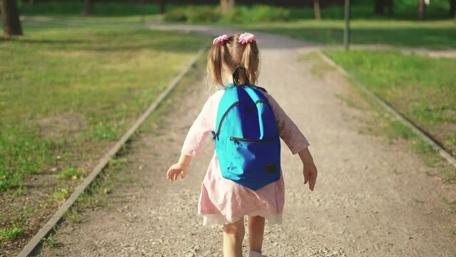 back to school. a little girl with a backpack runs through the green park to school along the path. education kid dream concept. a sun small child with a backpack back view runs the park to school