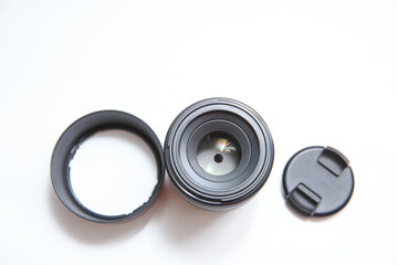 A small photographic lens is separate from the camera on a white background. Elements of photographic equipment on white background. Lens complete with lens caps and lens hood.