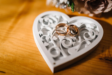 Two gold wedding rings on a wooden box in the shape of a heart. Top view. Wedding rings of the bride and groom. Engagement.