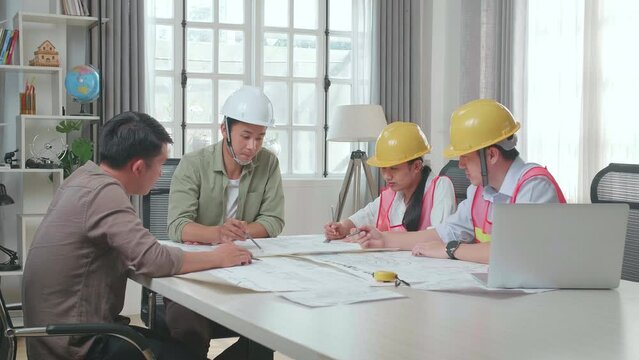 Three Asian Engineers With Helmets Presenting Work To A Man At The Office
