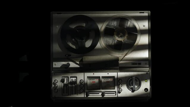old reel tape recorder plays magnetic tape record. Front view of old vintage tape recorder on black background, isolated object. rays of sun fall on recorder. concept of detective or documentary.
