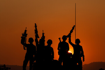 silhouette group of special forces sodiers hold the guns on tanks to indicative of their victory with the sunset background