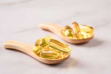 Wooden spoons with dietary supplement omega 3 on marble table background. Oil filled capsules, cod liver oil pills. Selective focus