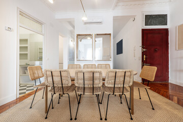 Living room with oval wood dining table, wicker chairs, natural fiber rug and hardwood floors, wall mirrors and access to a bathroom