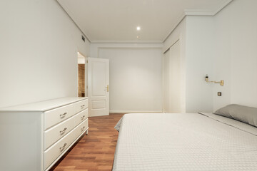 Bedroom with large double bed, white wooden chest of drawers with six drawers and wooden floors