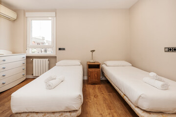 Bedroom with twin beds with white duvet, white chest of drawers and chestnut wood floors