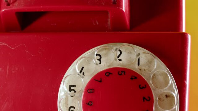 Close up of dialing on old vintage red dial telephone. rotary dialer spins and dials number. Pulse dialing. backing with numbers is dirty from antiquity.