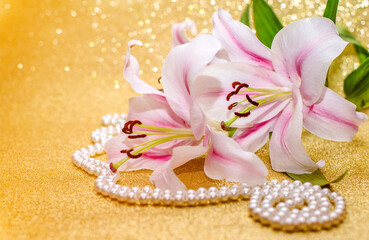 White lilies and pearl necklace on a shiny gold background
