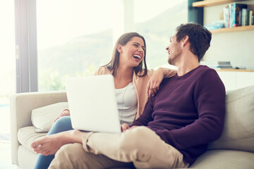 Sharing an online laugh. Shot of a smiling young couple using a laptop while relaxing on the sofa at home.