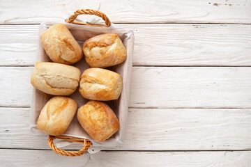Fresh wheat buns in a wicker basket on white wooden table