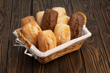 Fresh wheat and rye bread in a wicker basket on a brown wooden table