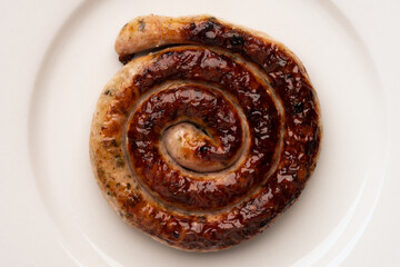 Fried spiral sausage on a white plate close up