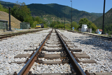 Low angle of railways covered with pebbles leading to green mountains covered with forests