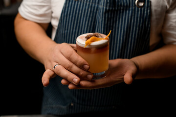 male hands gently hold glass with foamy alcoholic cocktail decorated with zest