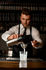 Fototapeta na wymiar bartender holds shaker and pours white liquid into glass through sieve