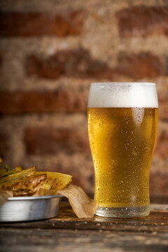 Cold beer in a long glass alongside a metal bowl of french fries on a bar counter with copy space