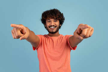 Cheerful curly eastern guy pointing at camera