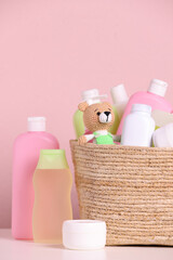 Obraz na płótnie Canvas Baby cosmetic products, bath accessories and toy in wicker basket on white table against pink background