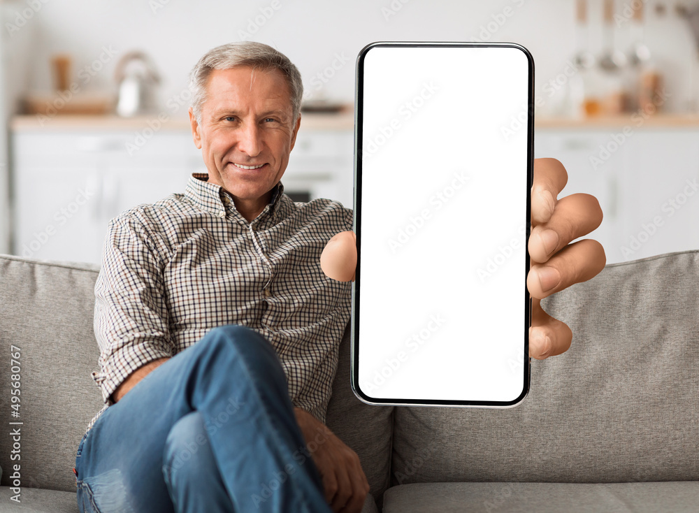 Poster cool mobile application. smiling senior man showing cellphone with white blank screen, sitting on so