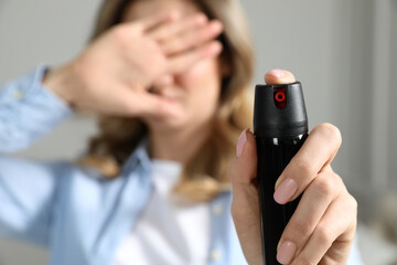 Young woman covering eyes with hand and using pepper spray at home
