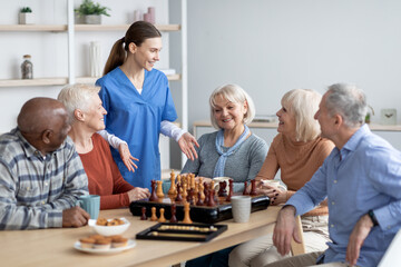 Friendly nurse talking to elderly people playing table games