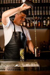male bartender skillfully pours a cocktail from one shaker cup to another