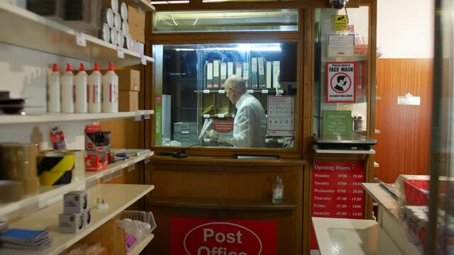 A post master in a post office labelling parcels behind the shop counter