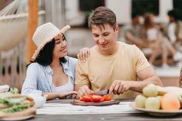 Young diverse couple cooking together near camper van outdoors, cutting vegetables for breakfast, enjoying camping trip