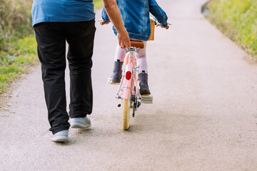 Anonymous grandfather teaching girl riding bicycle in countryside