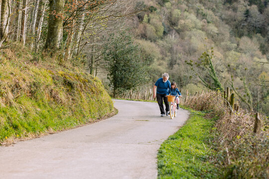 Grandfather teaching girl riding bicycle in countryside