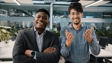 Two cheerful colleagues African man Arabian salesman looking at camera laughing joke funny business situation corporate prank in workspace appreciating good sense of humor rejoice positive atmosphere