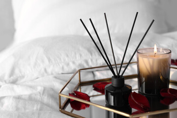 Aromatic reed air freshener, red petals and candle on bed, space for text
