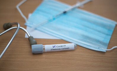 Closeup of a COVID omicron variant test tube on the table with a facemask and a stethoscope on it