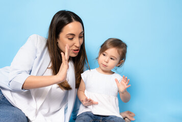 Picture of happy young woman mother with her little girl child daughter sitting isolated over blue background.