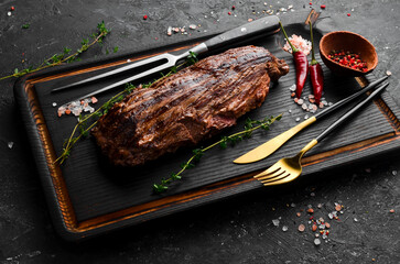 Juicy veal steak with spices on a black wooden board. Top view. Grilled meat.