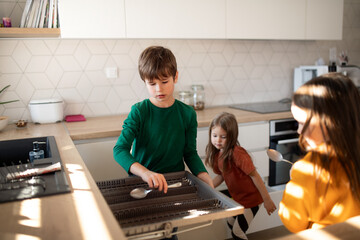 Three little chidlren helping with dishes in kitchen at home.
