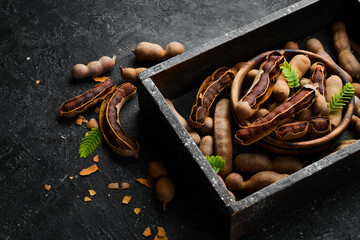 Exotic tamarind fruits in a box. Top view. On a stone background.
