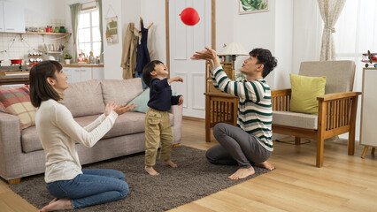 cheerful asian dad, mom and preschool son enjoying playing together with a red balloon at home....