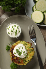 Delicious zucchini fritters with sour cream served on wooden table, flat lay